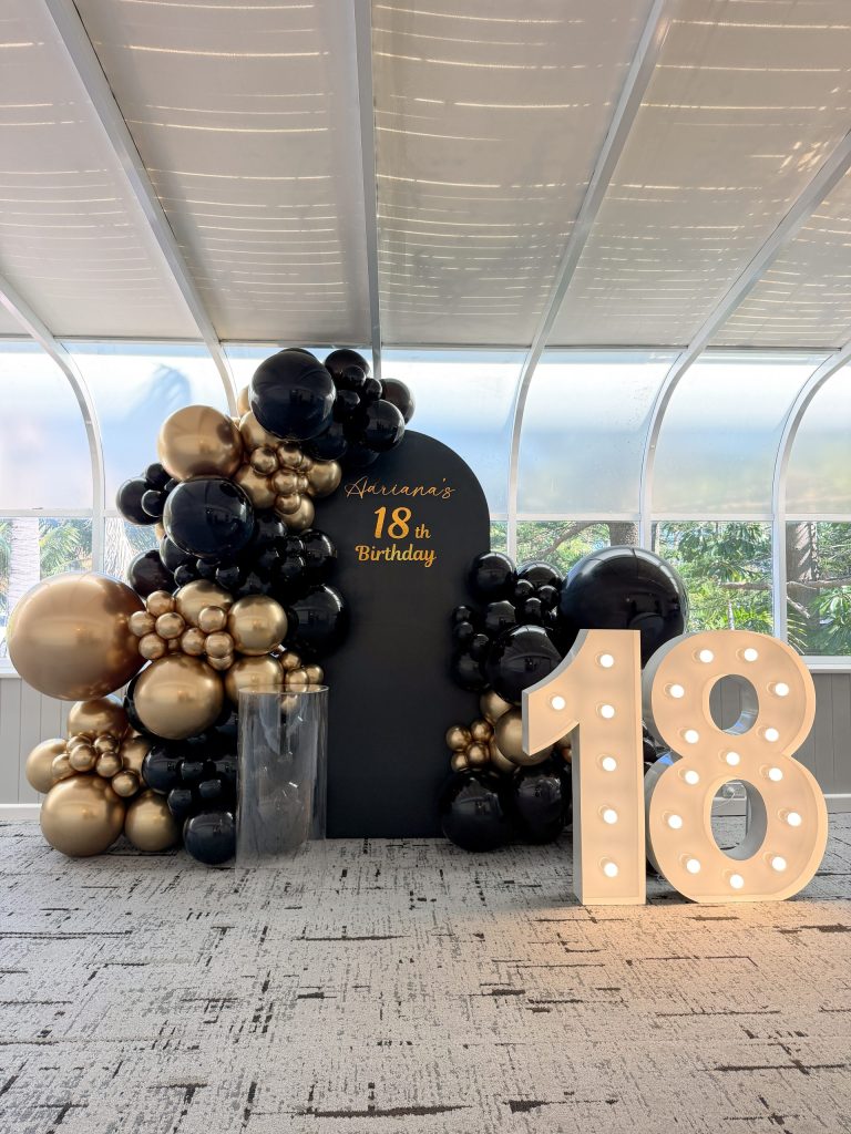 Elegant 18th birthday setup featuring glossy black balloons, metallic gold accents and illuminated number 18 lights